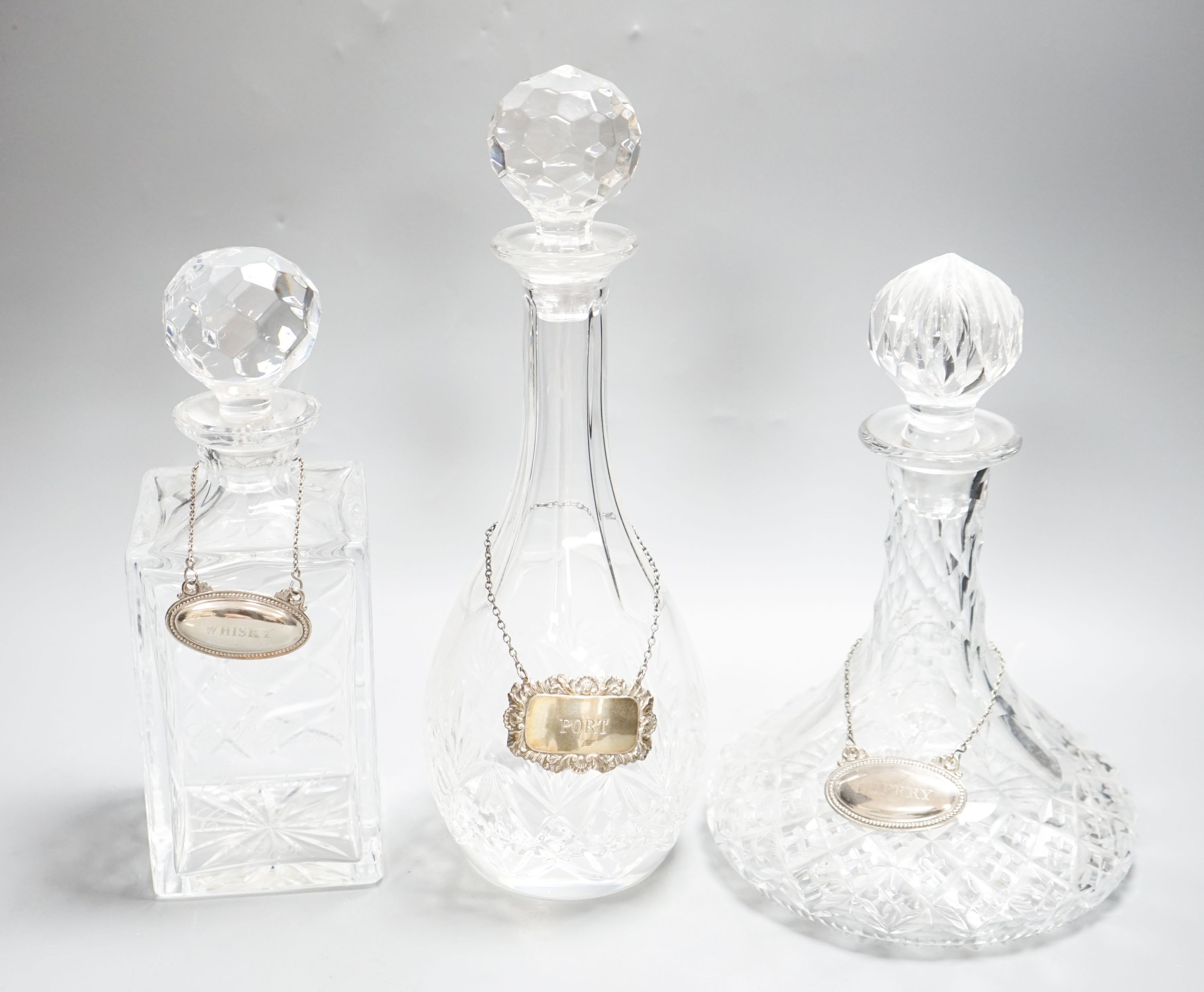 Three glass decanters, white metal labels